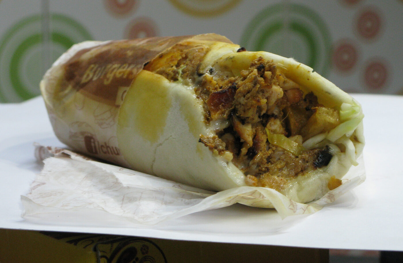 Chicken shawarma wrap cut on a board, tomato and pickle showing